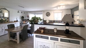 A kitchen with a wooden table and chairs, a hanging light fixture, and a clock on the wall. - Maison de charme conviviale (Montgivray)