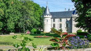 A castle with a round tower, surrounded by well-maintained gardens and trees. - Maison de charme conviviale (Montgivray)