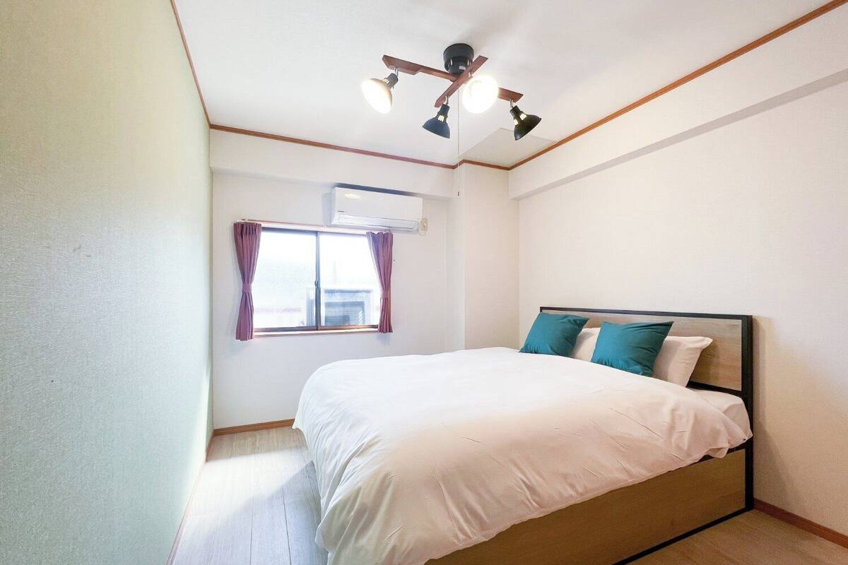 A bedroom with a bed, a window with curtains, an air conditioning unit, and a ceiling fan.