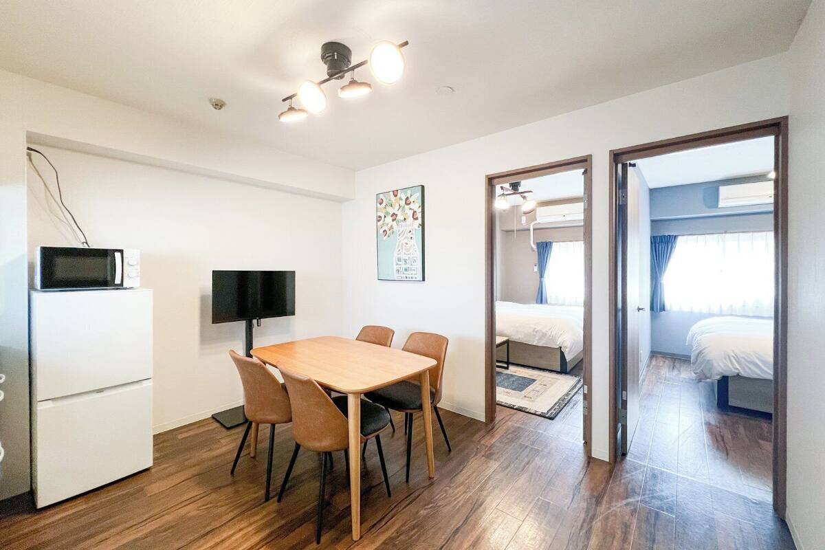 A compact hotel room with a wooden dining table, a flat-screen TV, a microwave, and a bunk bed.