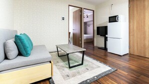 A living room with a sofa, a small table, a TV, and a refrigerator. - Alita Mansion Kyobashi (Osaka)