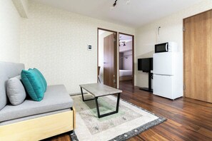 A living room with a sofa, a small table, a TV, and a refrigerator. - Alita Mansion Kyobashi (Osaka)