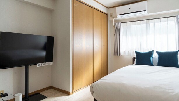 A hotel room with a bed, a TV, a wardrobe, and an air conditioning unit. - Alita Mansion Kyobashi (Osaka)