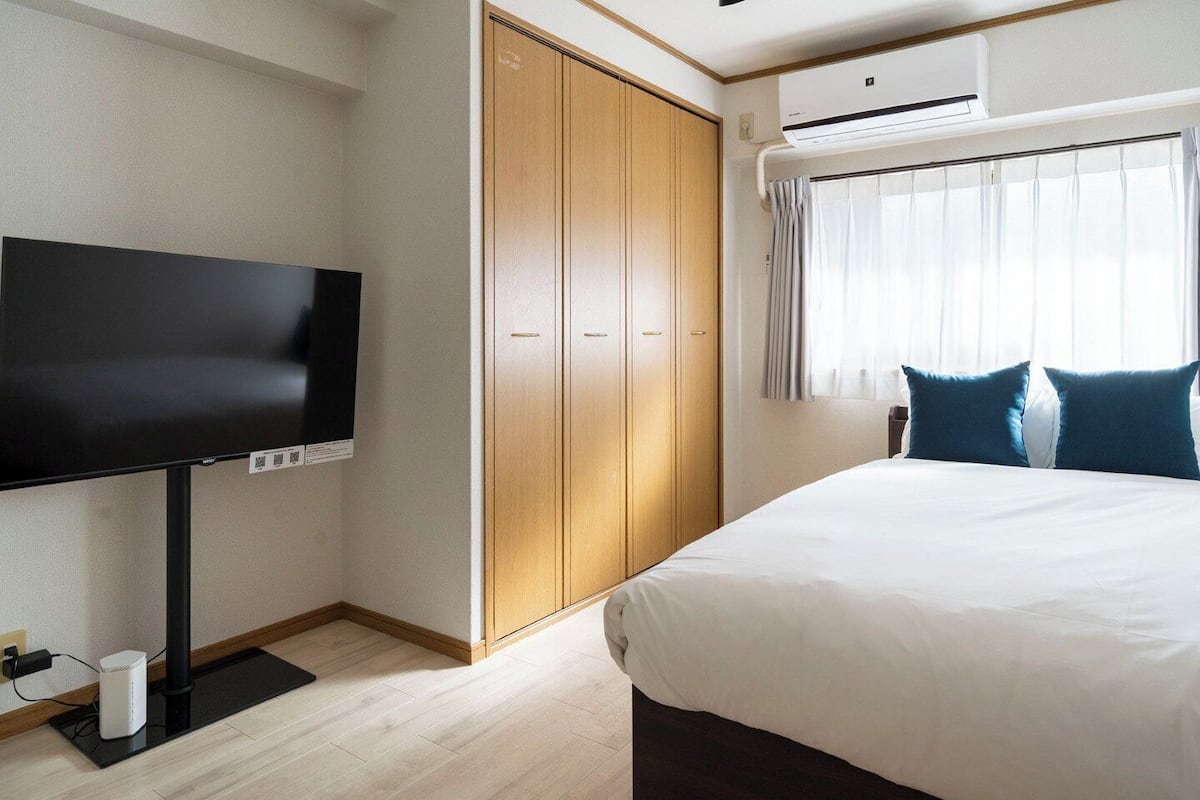 A hotel room with a bed, a TV, a wardrobe, and an air conditioning unit.