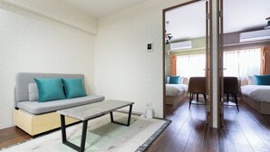A modern living room with a sofa, a coffee table, and a dining area with chairs. - Alita Mansion Kyobashi (Osaka)