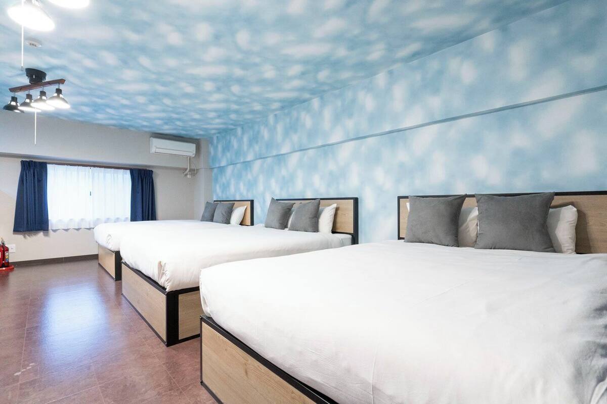 A hotel room with two beds, a window with curtains, a ceiling fan, and a fire extinguisher.