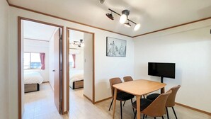 A hotel room with a wooden dining table, four chairs, a flat-screen TV, and a painting on the wall. - Alita Mansion Kyobashi (Osaka)