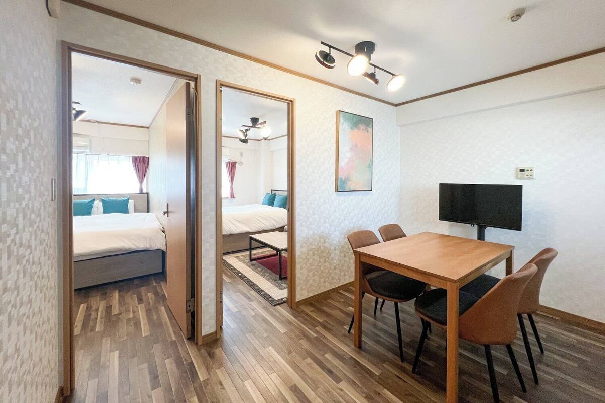 A room with a bed, a desk, chairs, a TV, and a painting on the wall.