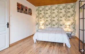 A bedroom with a bed, wooden flooring, a wall with a bamboo wallpaper, two bedside lamps, and a door.