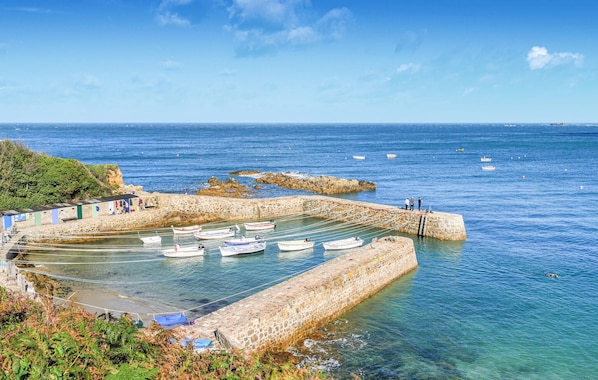Un port côtier où des bateaux sont amarrés, avec des murs de pierre et un ciel bleu dégagé.