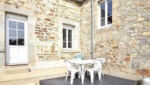 A stone building with a patio area, white plastic chairs, and a metal pot. - Cozy home in Saint-Christophe-du-Foc with WiFi (Saint-Christophe-du-Foc)