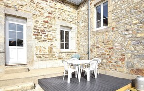 Un bâtiment en pierre doté d’un patio, de chaises en plastique blanc et d’un pot en métal.