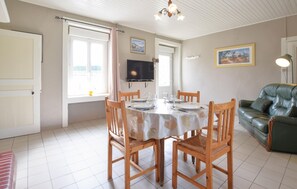 A dining area with a round table, wooden chairs, a television, and a green sofa.