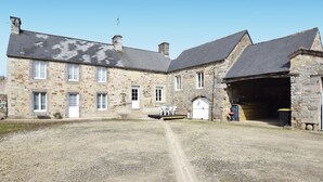 A stone building with a gravel driveway, a white door, and a small outdoor seating area. - Cozy home in Saint-Christophe-du-Foc with WiFi (Saint-Christophe-du-Foc)