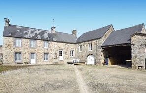Un bâtiment en pierre avec une allée de gravier, une porte blanche et un petit espace extérieur aménagé pour s’asseoir.