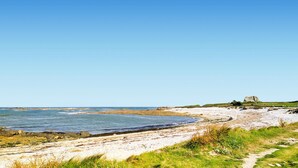 A coastal landscape with a clear sky, a sandy beach, rocky outcrops, and a distant building. - Cozy home in Saint-Christophe-du-Foc with WiFi (Saint-Christophe-du-Foc)