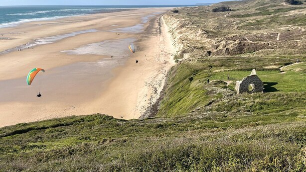 A beach with a dune system, a lighthouse, and a parasail in the distance. - Beautiful home in Barneville-Carteret with WiFi (Barneville-Carteret)