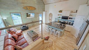 Un salón espacioso con suelo de madera, un sofá, una mesa de centro y vistas a la playa a través de una ventana.