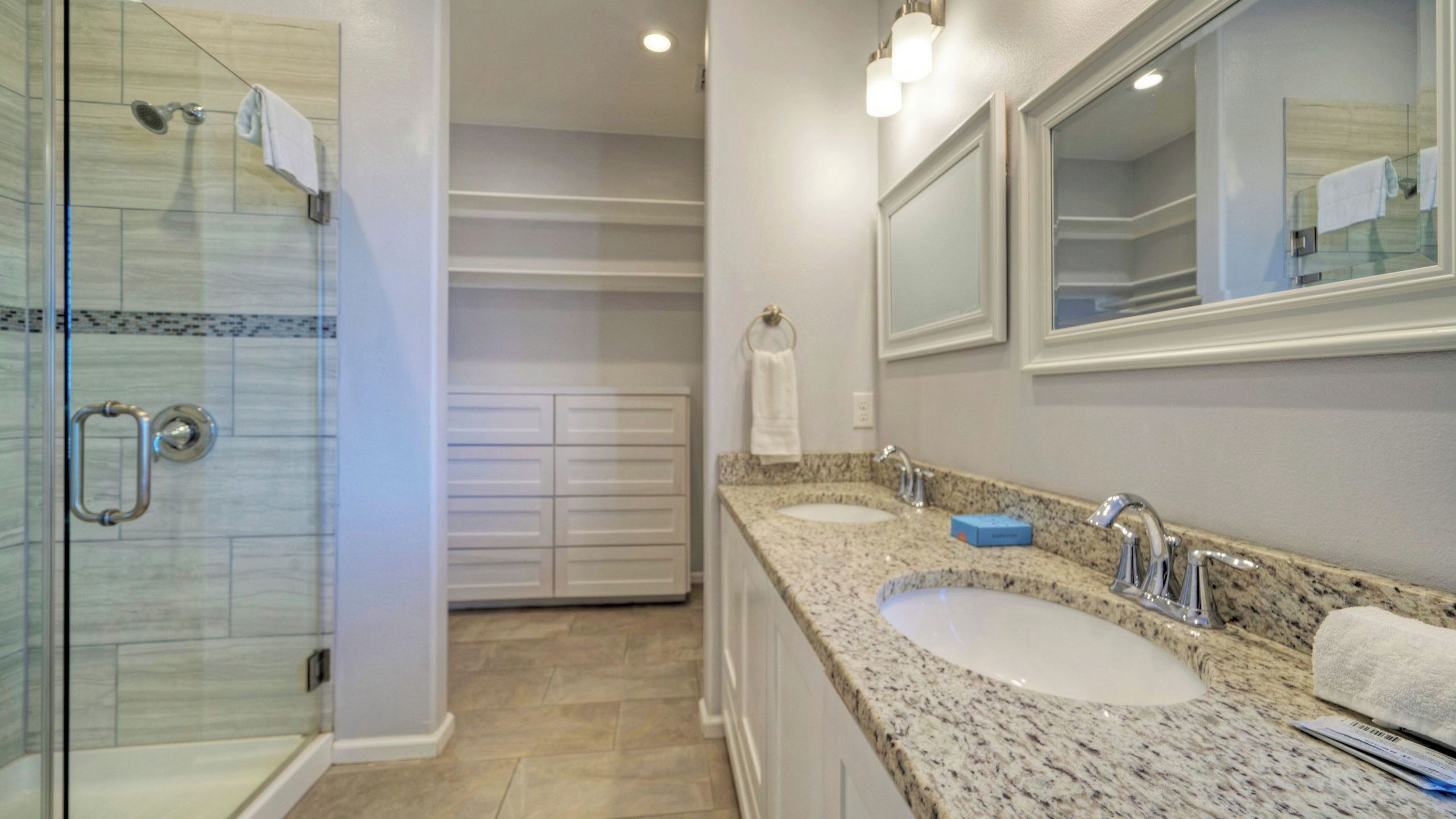 A bathroom with a glass shower enclosure, two sinks with granite countertops, and a large mirror.