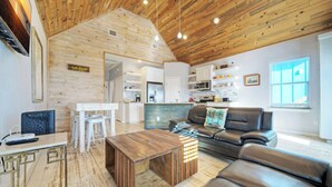 Un amplio salón con techo de madera, un sofá, una mesa de centro y una cocina al fondo.