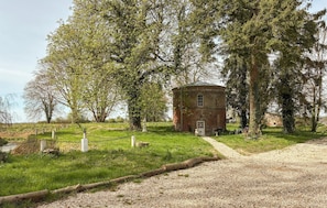 Un bâtiment rustique en briques, entouré d’une végétation luxuriante et bordé d’un chemin de gravier.