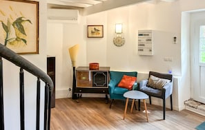 Un salon avec un escalier, un climatiseur fixé au mur, une horloge et un tableau encadré.