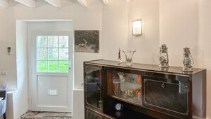 Una habitación con una puerta blanca, una ventana con vistas, un aparador de madera oscura con puertas de cristal y una lámpara fijada a la pared.