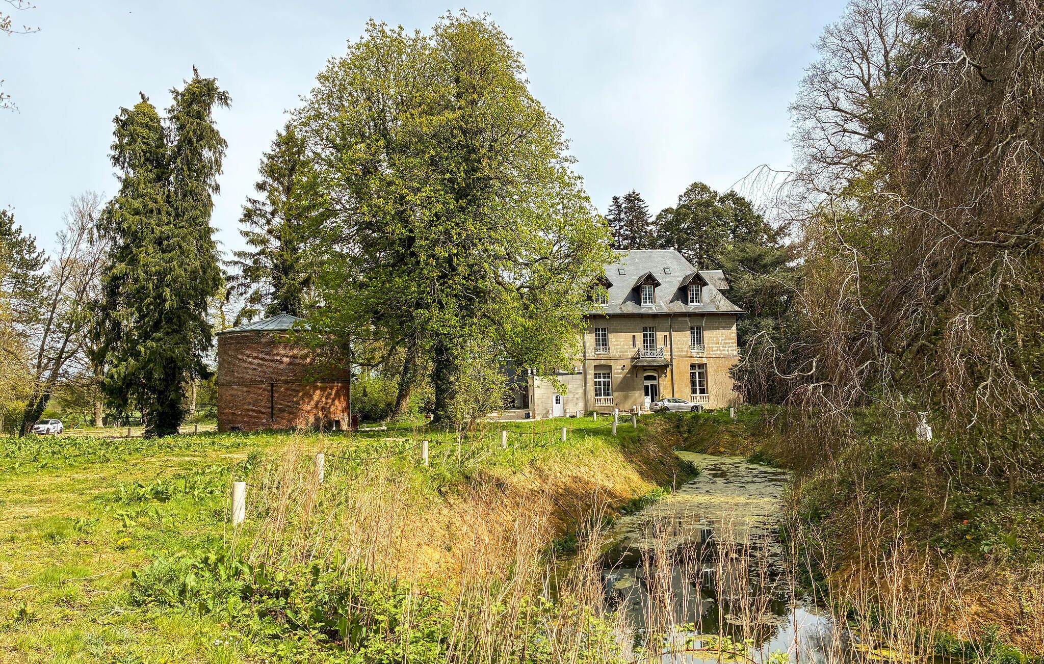 A large stone building with a prominent entrance, surrounded by lush greenery and a small stream.