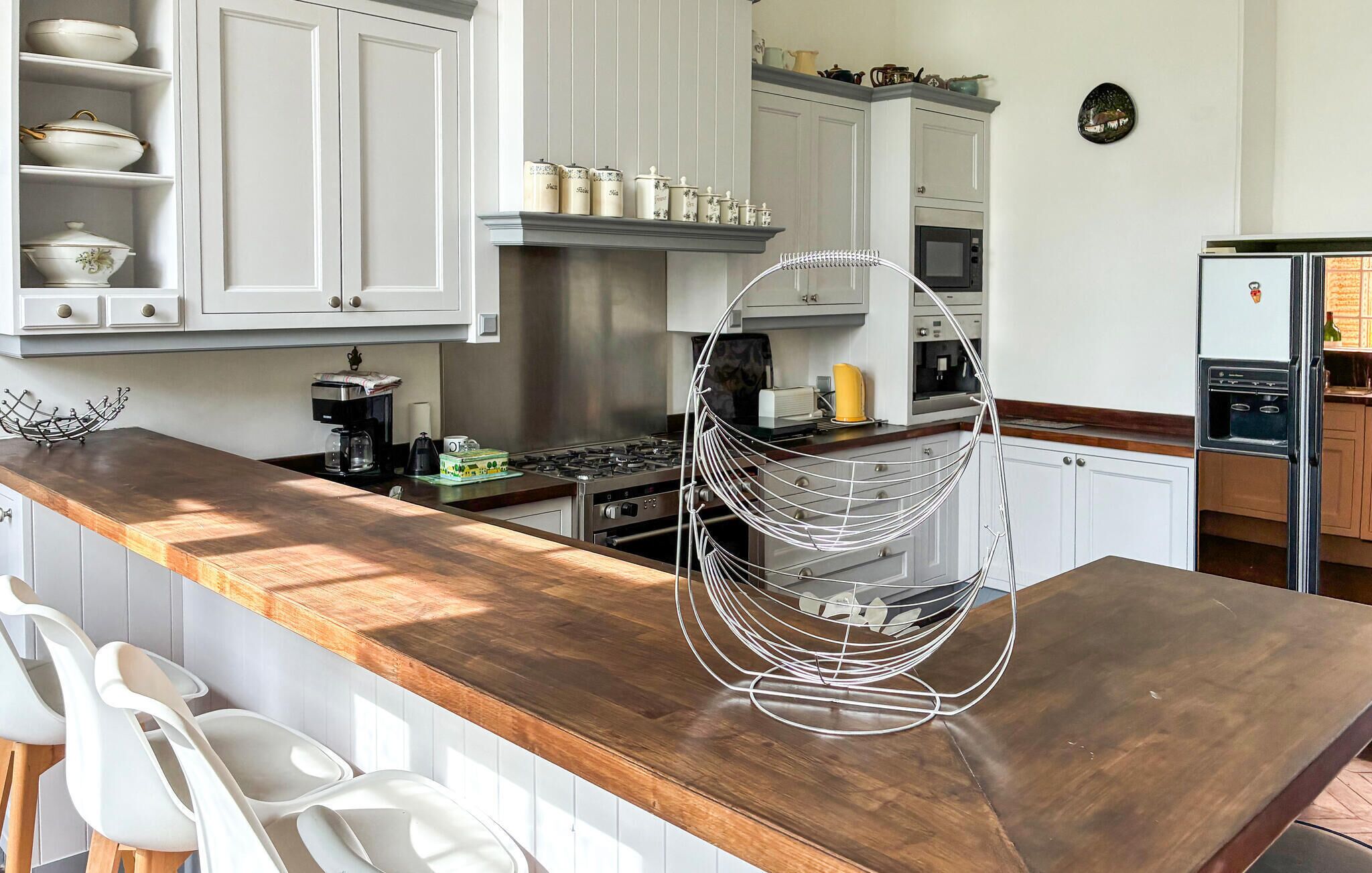 A kitchen with white cabinets, a wooden countertop, a hanging wire rack, and a refrigerator.