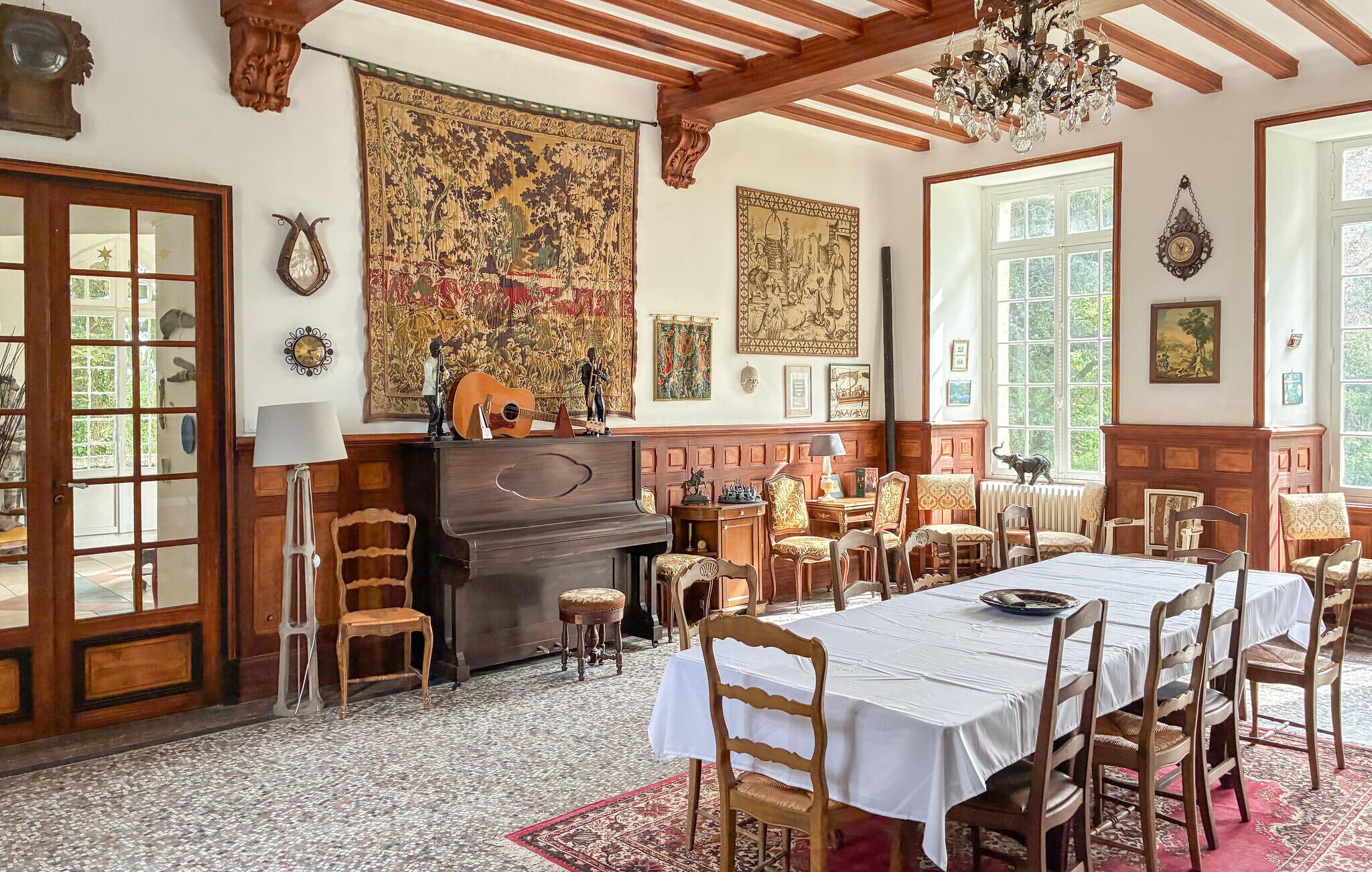 Ein Esszimmer mit Klavier, Holzsesseln, einem Tisch für vier Personen und einem großen Wandteppich.