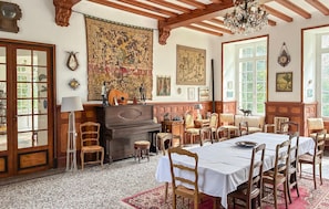 Ein Esszimmer mit Klavier, Holzsesseln, einem Tisch für vier Personen und einem großen Wandteppich.