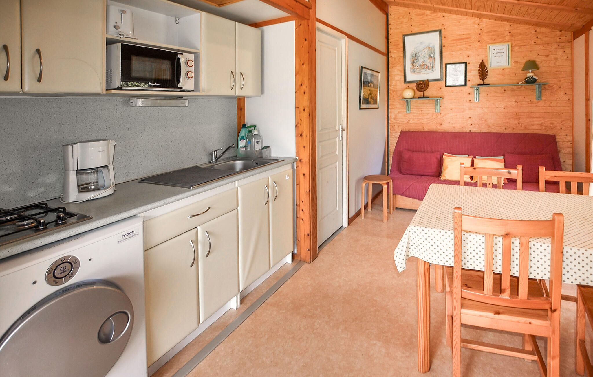 A compact kitchen with a microwave, coffee maker, and a washing machine. There is a dining area with a table and chairs, and a red sofa.