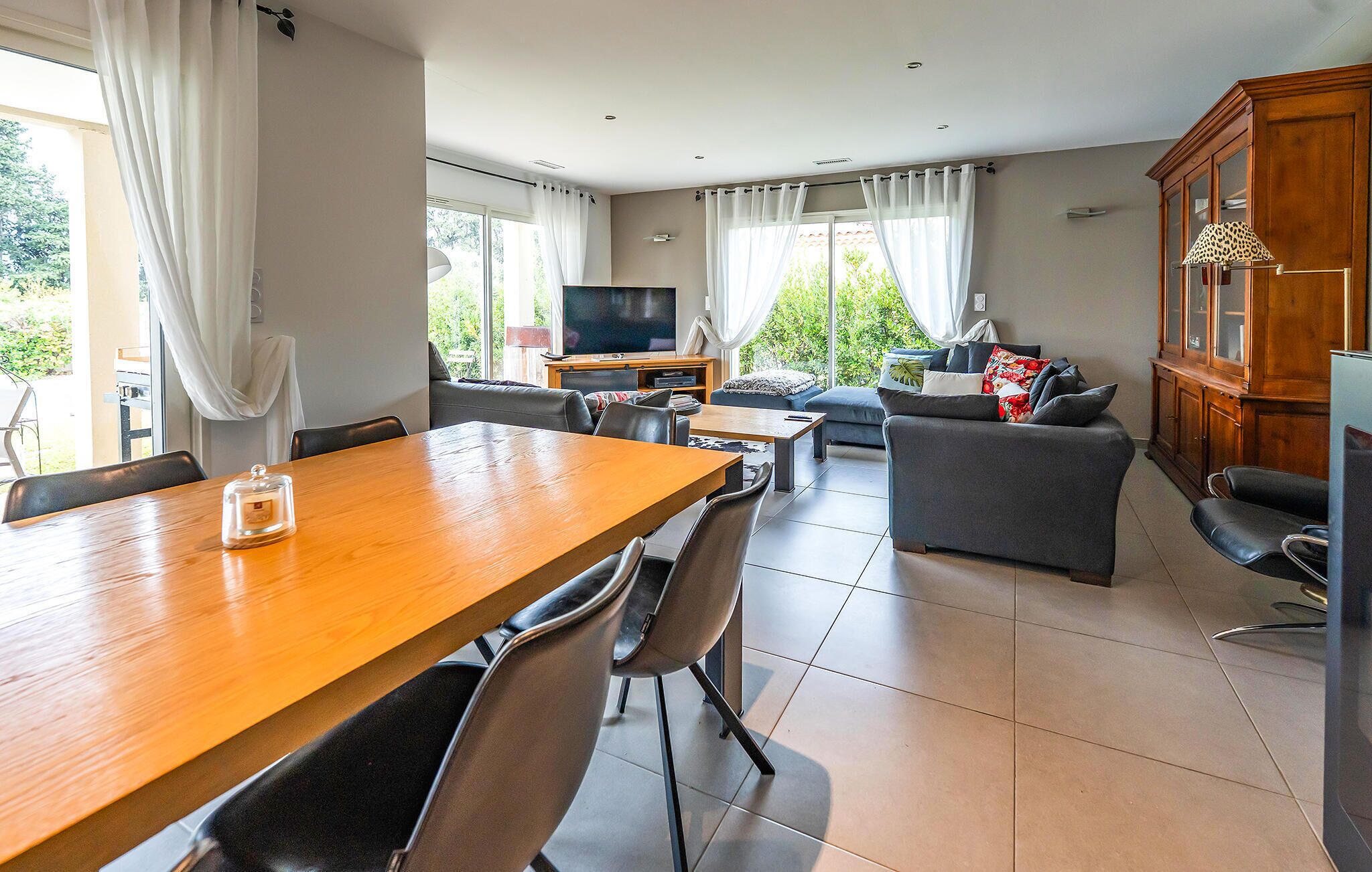 A spacious living area with a wooden dining table, grey sofa, and a TV.