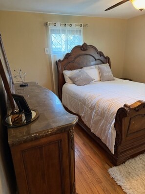 Une chambre à coucher avec un lit en bois, une table de chevet, un miroir et une fenêtre avec des rideaux.