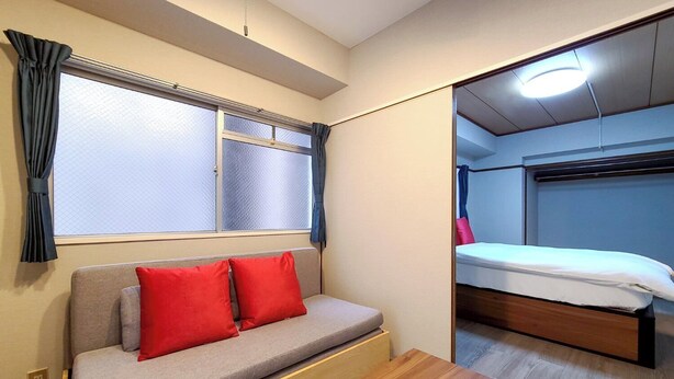 A room with a sofa, a wooden table, a bed, and a window with curtains. - Mansion Castle (Osaka)