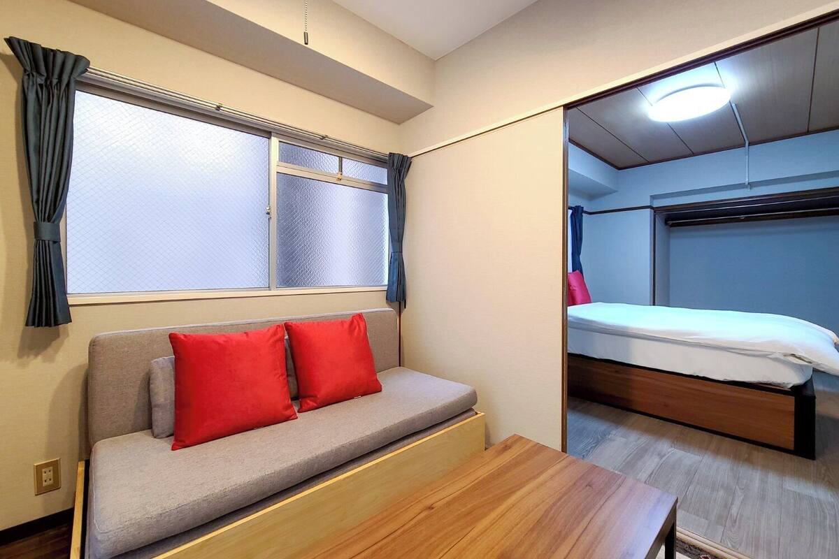 A room with a sofa, a wooden table, a bed, and a window with curtains.
