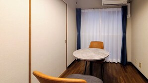 A small room with a round table and two chairs, an air conditioning unit, and a window with curtains. - Mansion Castle (Osaka)