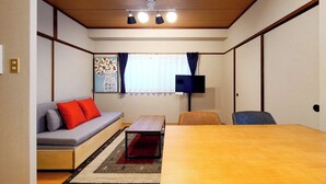 A compact room with a sofa, a small table, a TV, and a window with curtains. - Mansion Castle (Osaka)