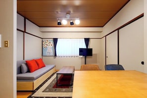Ein kleines Zimmer mit Schlafsofa, Tisch, Fernseher und einem fenster mit Vorhängen.