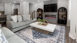 A modern living room with a grey sofa, a white coffee table, a patterned rug, a fireplace, and a TV mounted on the wall. - Charming 3-bedroom townhome with 2 car garage in vibrant Charlotte. (Charlotte)