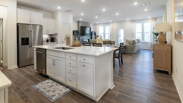 A modern kitchen with a central island, stainless steel appliances, and a dining area with a sofa and table. - Charming 3-bedroom townhome with 2 car garage in vibrant Charlotte. (Charlotte)