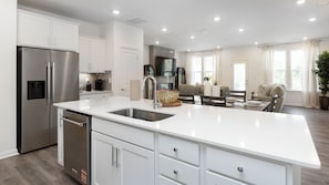 A modern kitchen with a stainless steel refrigerator, white cabinetry, and a large island with a sink. - Charming 3-bedroom townhome with 2 car garage in vibrant Charlotte. (Charlotte)