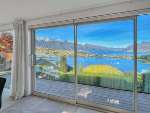Ein Zimmer mit einer großen Schiebetür, die auf einen Balkon mit herrlichem Blick auf einen See, Berge und eine kleine Stadt führt.
