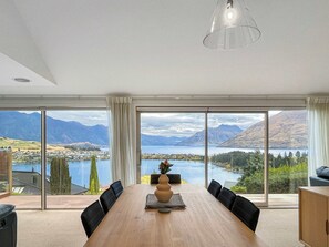 Ein Essbereich mit Holztisch, schwarzen Stühlen, einer Vase und Blick auf einen See und Berge.