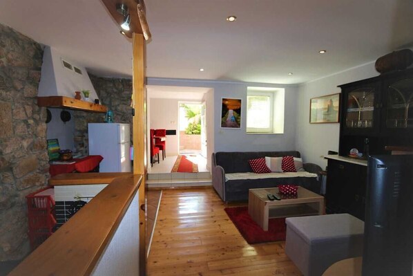 A cozy living room with a wooden floor, a sofa, a coffee table, and a kitchen area with a refrigerator.