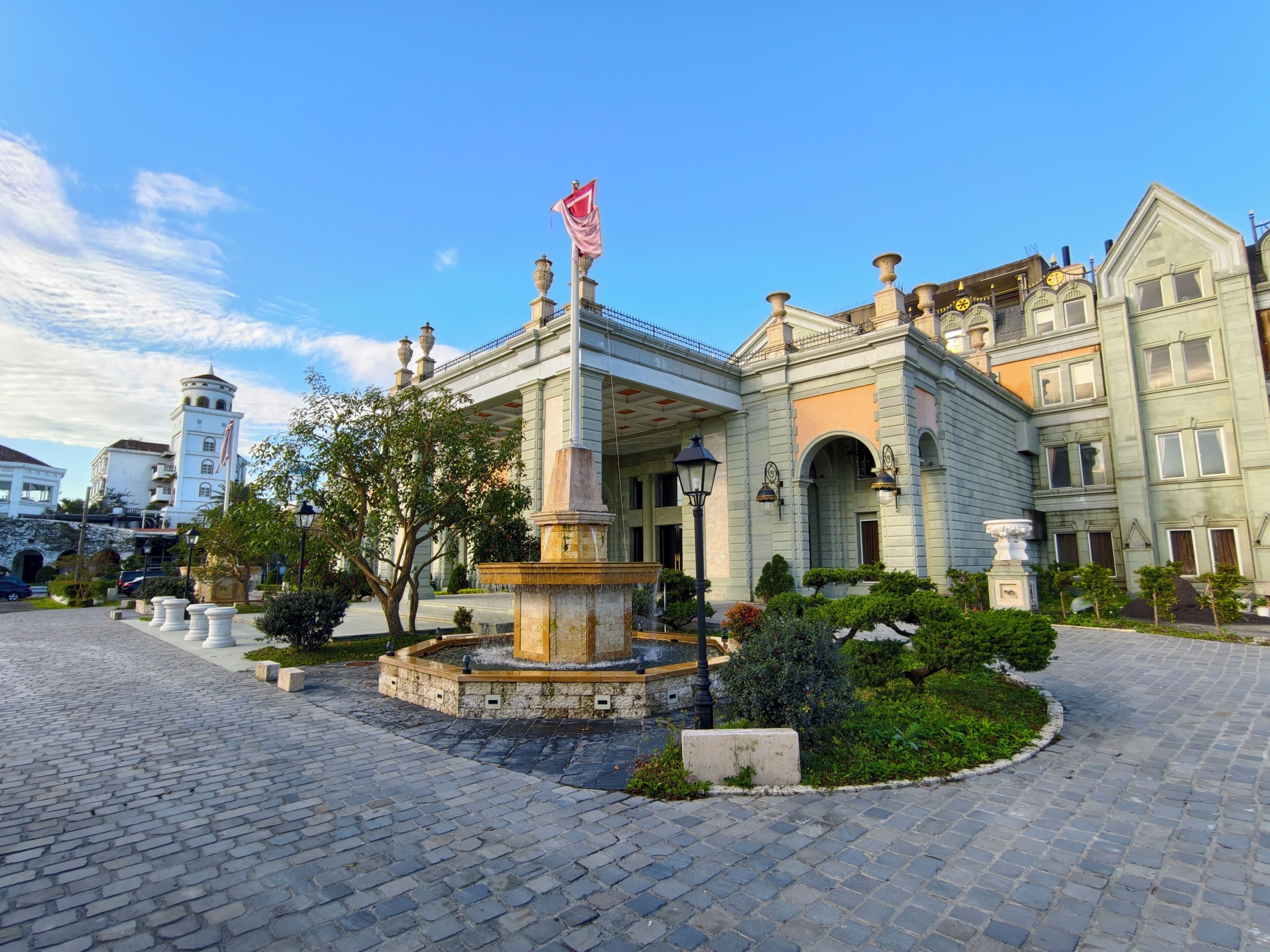 A historic building with a fountain, cobblestone courtyard, and a flag.