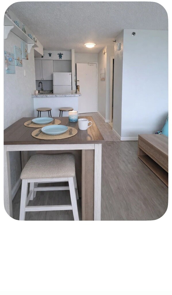 A compact kitchen with a dining area, a small stool, and a bench. - OCEAN VIEW Condo with pool (Daytona Beach)