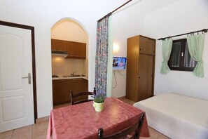 Ein kleines Zimmer mit Esstisch, Bett, Fernseher und Küchenzeile.