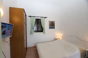 A bedroom with a bed, a wooden door, a window with curtains, a wall-mounted TV, and a small bedside table with a lamp. - Apartment Dunato Anita (Silo - island Krk)