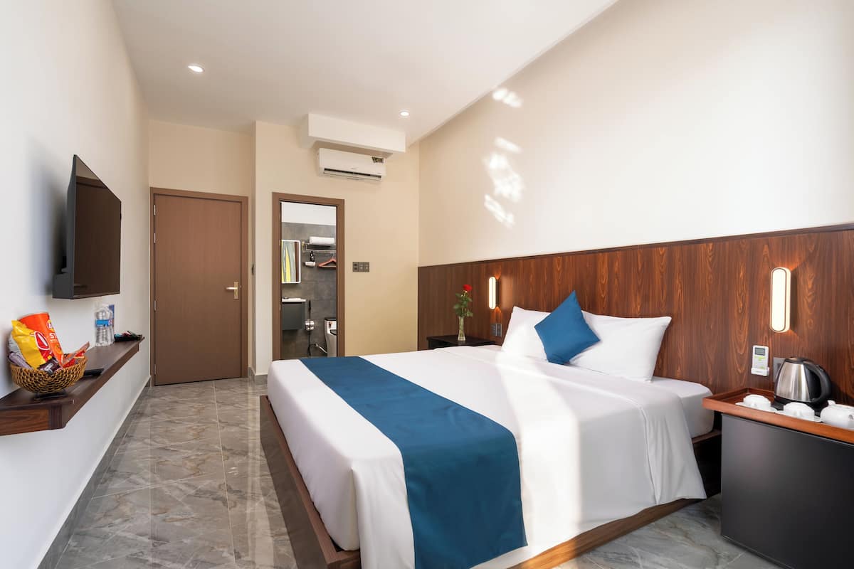 A hotel room with a bed, bedside table, TV, and a bathroom visible through an open door.
